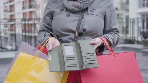 Close-up of Female Caucasian Hands Opening Empty Wallet. Unrecognizable Woman with Shopping Bags alt