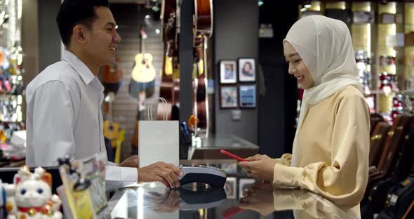 Young muslim woman use smartphone paying over contactless transaction machine
