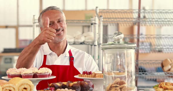 Happy Server Looking at Camera with Thumbs Up Behind Cakes alt