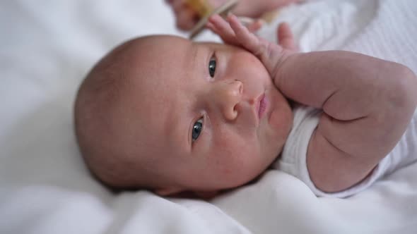Headshot Portrait of Cute Caucasian Newborn Infant with Grey Eyes Lying on Bed Looking Away alt