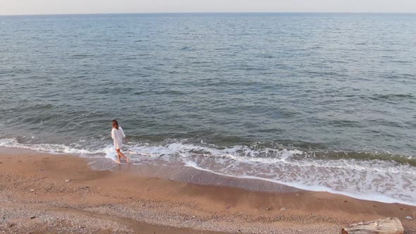 A Happy Girl in a Wet Shirt Runs Along a Sandy Beach and the Seashore
