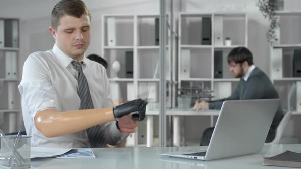 Businessman Taking Off Bionic Hand and Working on Laptop at Office Desk alt