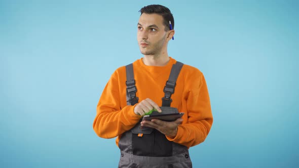 Worker in Industrial Work Clothes Looking Around and Writing on Tablet alt