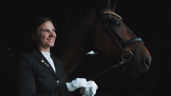 Horsewoman Standing With Her Dark Brown Horse Smiling And Putting On Her Gloves alt