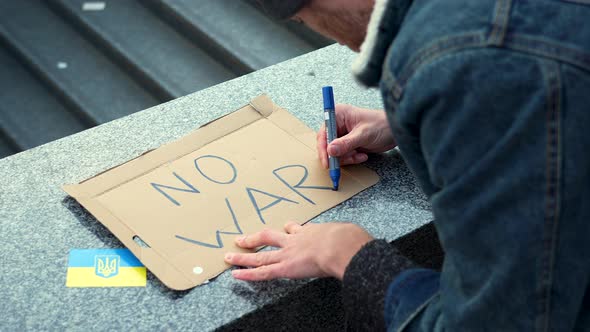 Man preparing a cardboard sign to protest against war in Ukraine, slow. alt