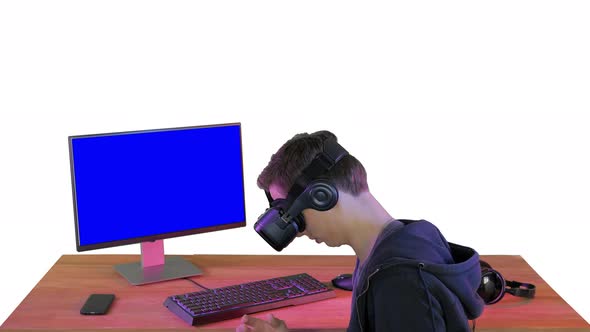 Young Gamer in Virtual Reality Headset Sitting at Table on White Background alt