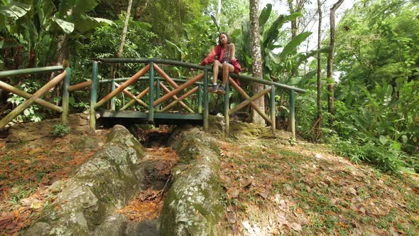stylish girl in red jacket sitting in a wooden bridge on a park alt