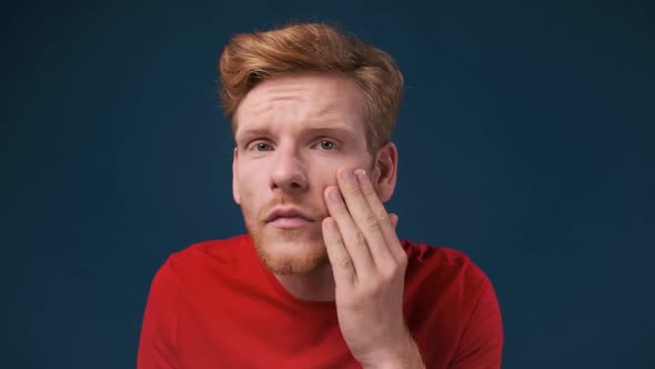 Face Close Up of a Young Ginger Man Looking at His Skin Problems Examining His Face Over Dark Blue alt