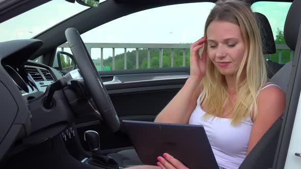 A Young Beautiful Woman Sits Relaxed in a Luxurious Car and Works on a Tablet - Closeup alt