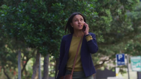 African american woman talking on smartphone while walking in street alt