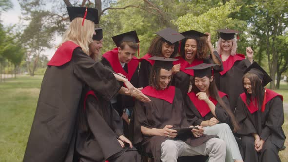Joyful Multiracial Graduates in Academic Gowns Working on Tablet Pc After Graduation Ceremony alt
