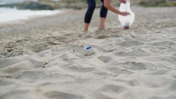 Closeup of a Woman's Hands Picking Up Plastic Trash Into a Bag on the Beach alt