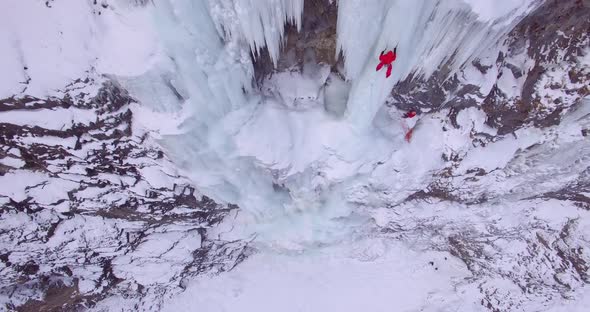 Aerial drone view of a man ice climbing on a frozen waterfall in the mountains. alt