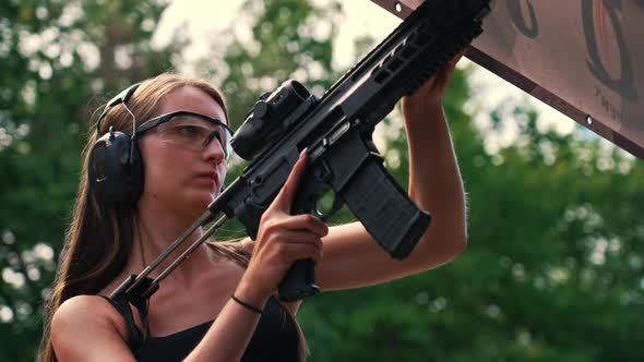 White Brunette Woman in Protective Gear Firing Submachine Gun on Training Ground alt