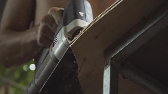 craftsman using an electric jigsaw to shape a skateboard deck from plywood by hand. No recognizable alt
