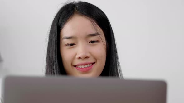 Close up face of Asian woman typing on laptop at home with happy face, working from home alt