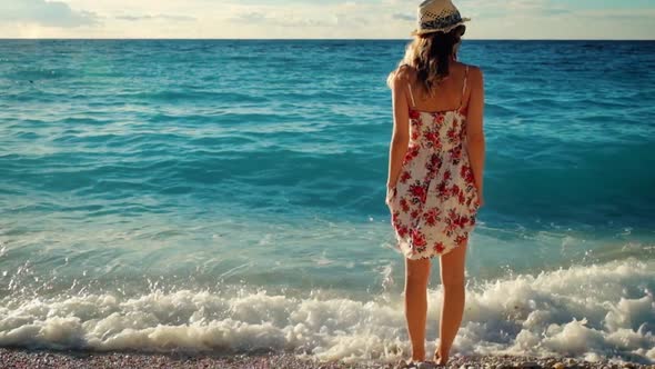 Young woman in dress standing on a beach at sunset over the sea.