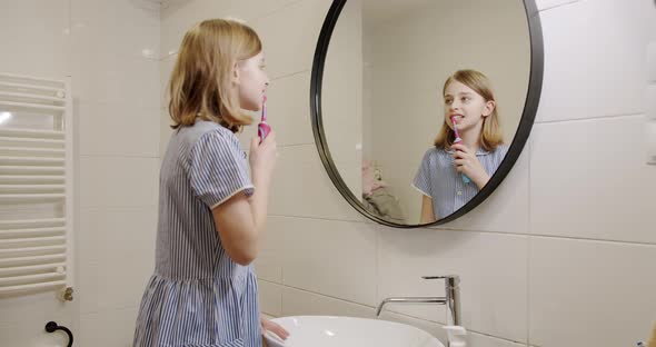 A Teenage Girl Brushes Her Teeth with an Electric Toothbrush in the Morning alt