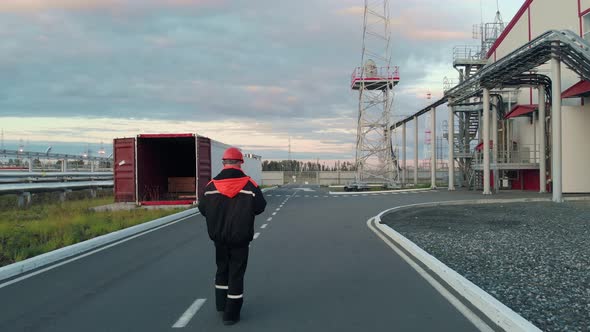 The Drone Flies After an Employee in Overalls and a Work Helmet Who Walks Along the Road Past alt