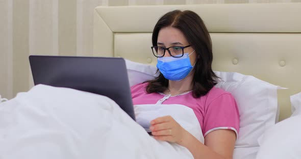 Woman with Medical Mask Working from Home on Laptop Computer During the Pandemic