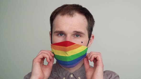 Portrait of a young man with a black heart on his cheek is putting on a rainbow face mask