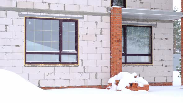 An unfinished house made of porous brick stands under the snow in winter - unfinished construction, alt