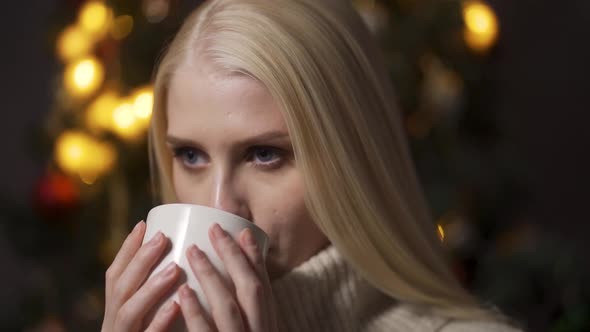 The Girl Sits Under the Christmas Tree and Drinks Cocoa