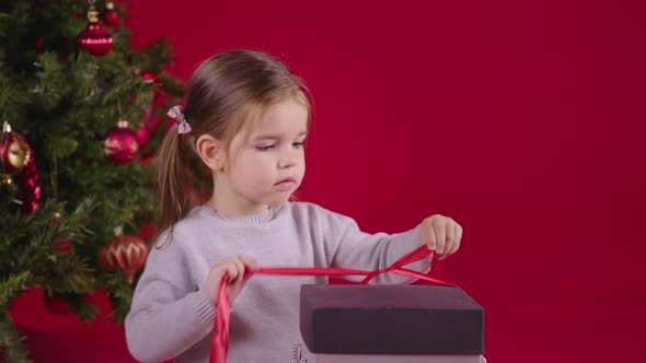 Little Cute Girl Opens Christmas Gift with Magic Light Inside Near Xmas Tree