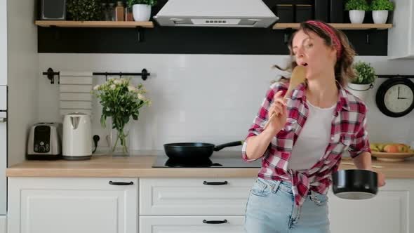 Carefree happy young woman housewife dancing alone cooking meal