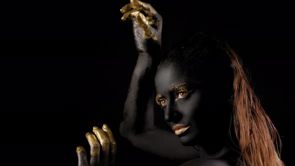 Portrait of a Young Woman with Black Paint on Her Face and Golden Hands and Lips alt