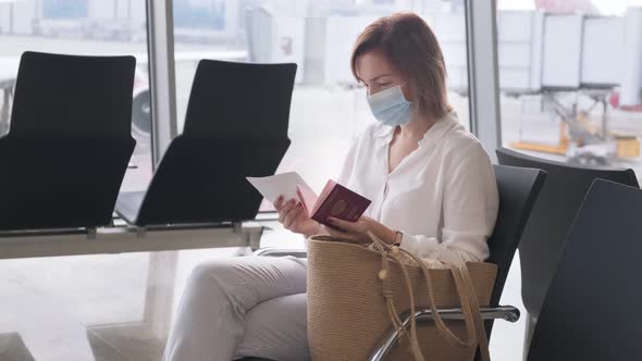 Woman in a Face Mask Checks Passport and Boarding Ticket in the Airport Terminal