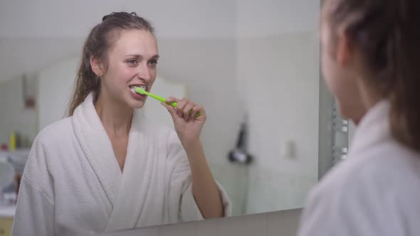 Reflection in Mirror of Young Slim Brunette Caucasian Woman Brushing Teeth with Toothbrush and alt