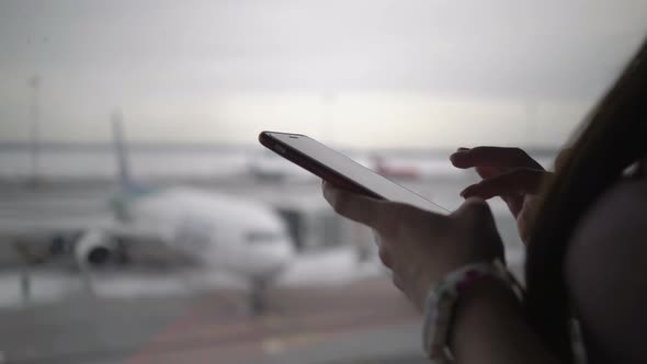Woman Using Mobile Phone at Airport Terminal and Waiting for Boarding the Plane alt
