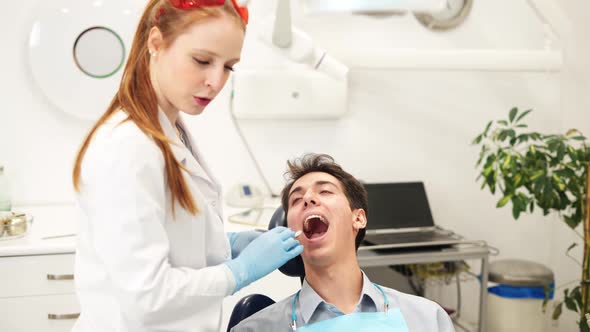 Young Female Dentist Examining Teeth of Male Patient with Mouth Mirror During Checkup alt