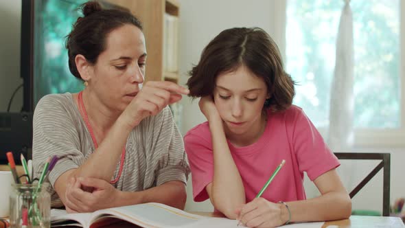 Mother helping her daughter to prepare homework at home alt