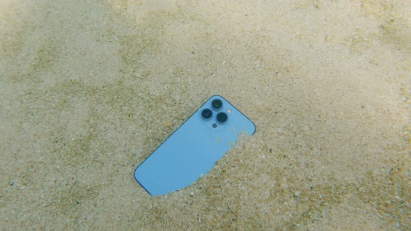 A Closeup of a Modern Fashionable Phone Lying on Bottom of the Ocean with White Sand