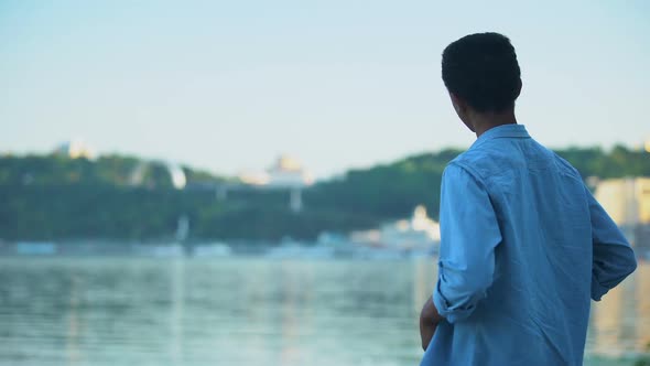 African American Guy Resting on River Embankment Enjoying City View, Landscape alt