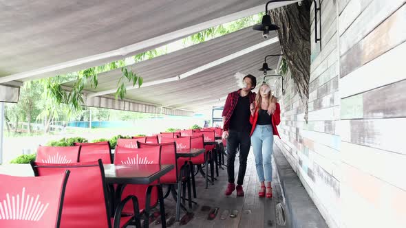Stylish Couple in a City. Two People Use the Electronic Cigarette alt