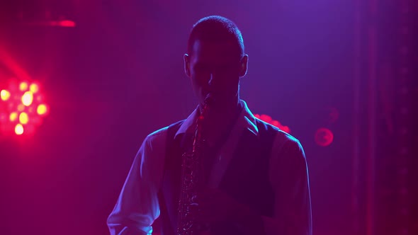Silhouette a Young Stylish Guy Plays the Saxophone on Stage. Dark Studio with Smoke and Neon alt