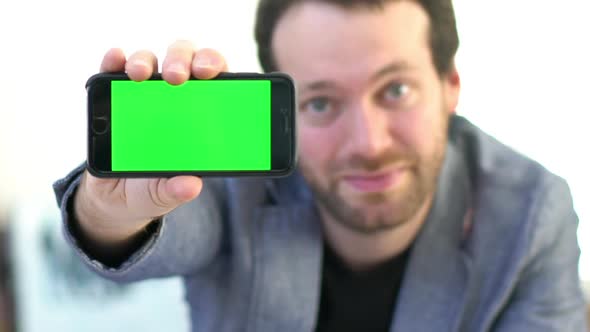Cheerful man showing smartphone display to camera alt