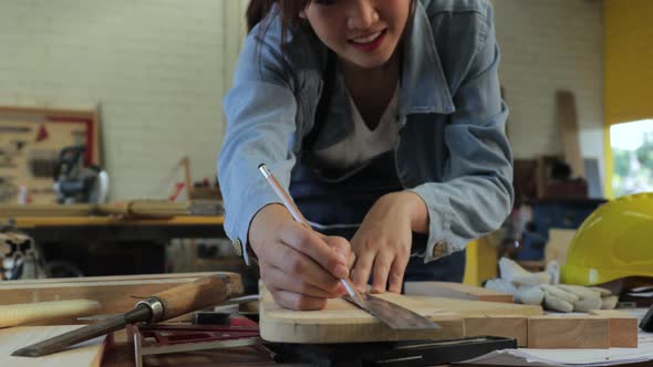 A female carpenter measures and marks line on a wooden plank.