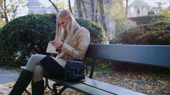 Girl Communicates in a Smartphone in a City Park on a Bench. alt