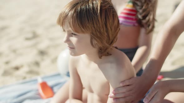 Slow Motion of Elder Sisters Hands Putting Sunblock on Boys Back alt