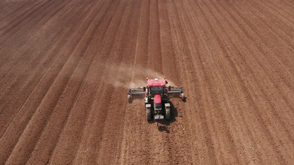 Red tractor flattening a field for seeding, Drone follow footage. alt