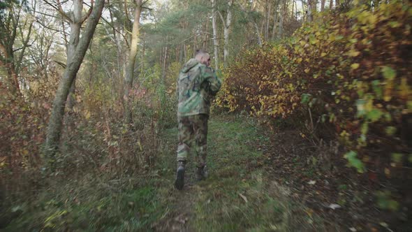 Back View of Soldier in Running with a Rifle in Forest and Looking Around alt