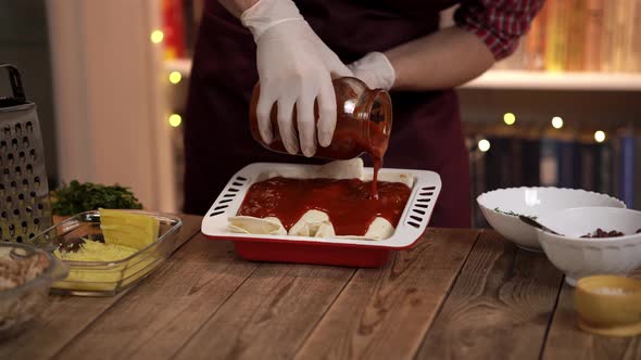 Closeup View of a Young Cook Standing at the Wooden Table and Pouring Tomato Sauce on Enchilada alt