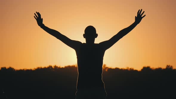 Silhouette of Man Against Sunset Raising Hands To Sides and Up. Slow Motion alt