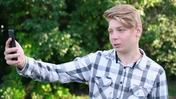 Young Teenager Man of Caucasian Ethnicity in a Gray Shirt in a Cage Stands on the Street in the alt