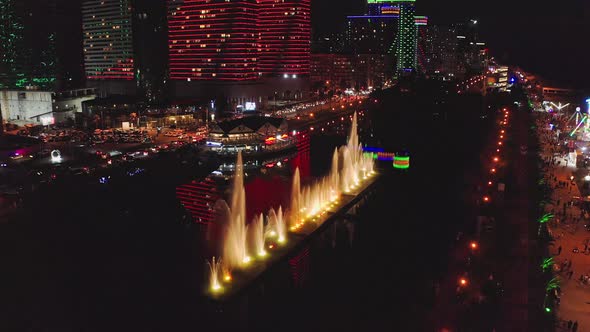 Illuminated Dancing Fountain Against Skyscrapers Of Night City alt