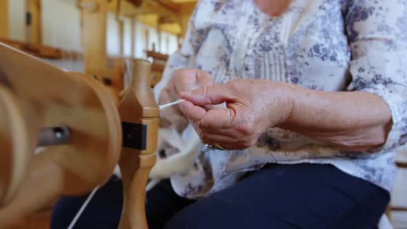 Senior woman pulling out thread and making yarn from weaving machine 4k alt